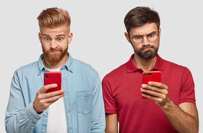 Horizontal,Shot,Of,Confused,Two,Males,Use,Mobile,Phoes,,Surfe Two adult males viewing mobile phone screens with confused looks.