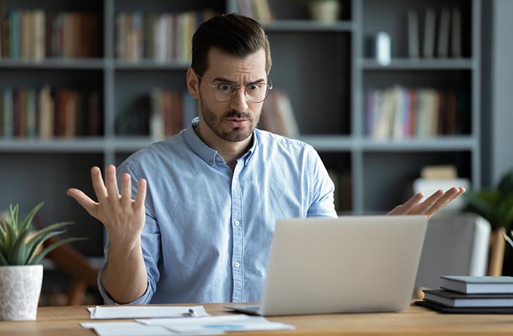 Unhappy young male in glasses looks shocked by problem on laptop screen..