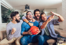 A group of male friends watching the March Madness men’s basketball tournament on TV at home.