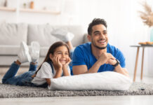 Father and daughter lying on the living room floor while watching a movie together at home.