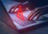 Hands typing on a laptop with an icon of a warning label depicting illegal activities.